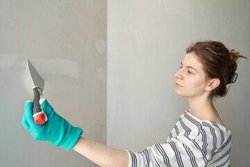 Young woman doing repair in the house in turquoise gloves. Repair the wall. Making primer with...