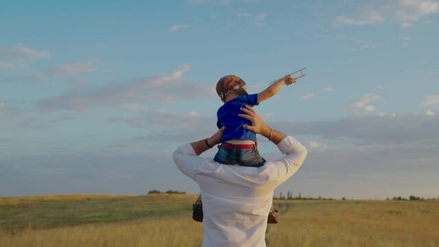 Dad walks with little kid, son on his shoulders, child dreams of becoming an airplane pilot, happy family. Son and dad play airplane pilot together. Weekend trip with child, fathers day. Slow motion