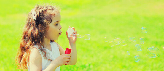 Portrait of little girl child blowing soap bubbles in summer day