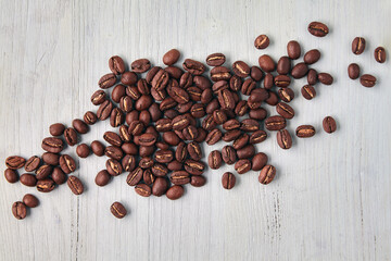 Randomly scattered roasted coffee beans on a white wooden background