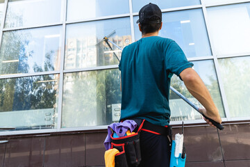 An employee of a professional cleaning service in overalls washes the facade and windows with...