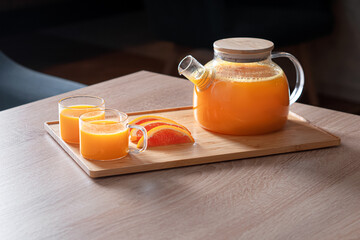 hot citrus drink in a glass teapot and mugs on the table