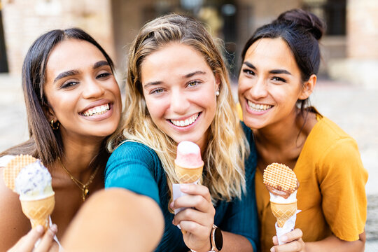 Diverse young women friends taking selfie together while eating an ice cream - Multiethnic female tourist having fun on summer vacation - Happy people concept