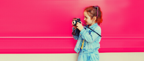 Little girl child with film camera taking picture looking away on pink background, banner blank...