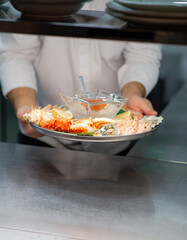 The chef serves a plate of cooked seafood on a bright table. Red salmon caviar, crab, shrimp, scallops, octopus