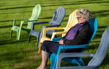 A woman sitting in one of five adirondack chairs on a pretty summer day. Shadows.