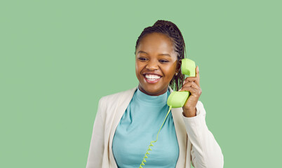 Joyful dark skinned woman talking on retro telephone with light green handset with wire isolated on...