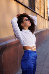 curly brunette girl smiling in cafe. Young woman enyoing sun in restaurant at window. white blouse. Sun in city. Fashionable asian girl with frizzly hair. Sun light in window