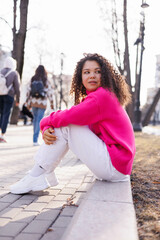 beautiful asia caucasian woman in pink sweater outdoors in street, spring, sun shining. Serious and sad, park trees