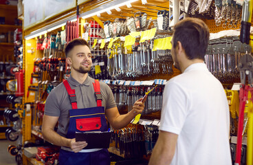Sales assistant at hardware store helping customer choose tools for home repairs. Salesman with...