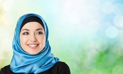 A young smiling muslim woman wearing a hijab over blur background.