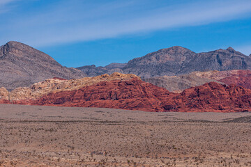 Las Vegas, Nevada, USA - February 23, 2010: Red Rock Canyon Conservation Area. Wide landscape with mountains of 3 colors, red, gray, yellow, under blue cloudscape. Dry sandy desert floor up front.