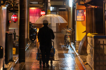 Man with umbrella pushes cart through rainy alley in historic district at night 