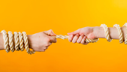 two hands in different positions are tied with a white wide rope on a yellow background close-up