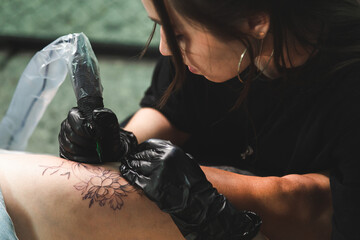 A professional tattoo artist makes a black and white tattoo on a woman's leg, applying in ink. The process of tattooing the skin.