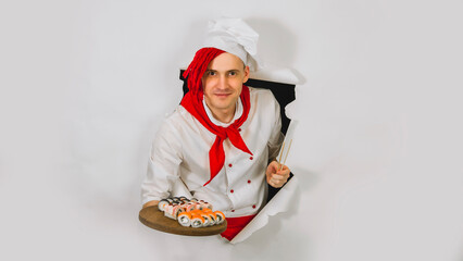 Young man dressed as chef holding wooden board with sushi rolls. Male cook with appetizing sushi rolls in hole of white background. Concept of fast food and takeaway.