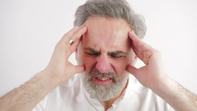 elderly man being visibly in pain because of a enormous headache heis having, white background, close up shot. High quality 4k footage
