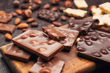 Board with pieces of tasty chocolate and nuts on dark background, closeup