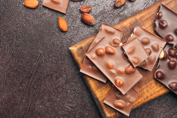 Board with pieces of tasty chocolate and nuts on dark background