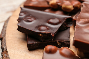Pieces of tasty chocolate with nuts on board, closeup