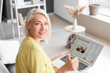 Beautiful mature woman with laptop showing thumb-up at home