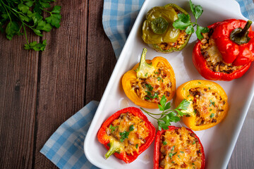 Stuffed peppers, halves of peppers stuffed with rice, dried tomatoes, herbs and cheese in a baking dish on a blue wooden table, top view. Vegetarian dish, stuffed vegetables