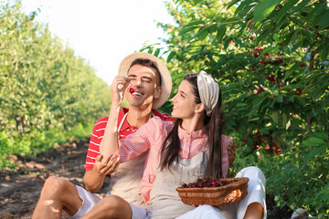 Young woman giving red cherry to her husband in garden