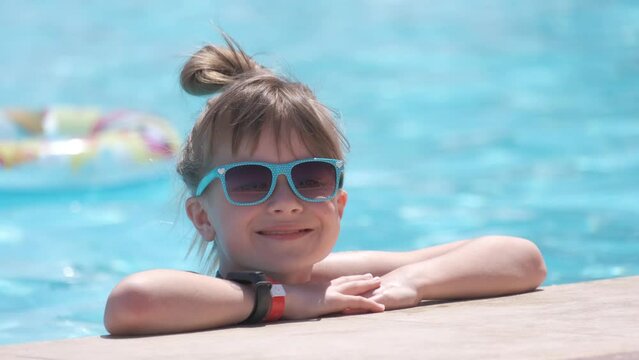 Young joyful child girl resting on swimming pool side with clear blue water on sunny summer day. Tropical vacations concept