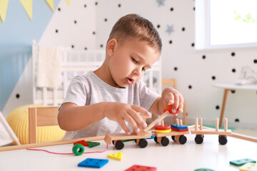 Cute little boy playing with wooden toys at table in room
