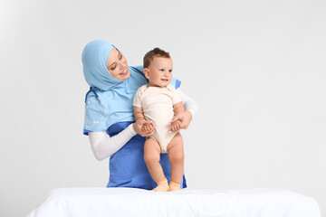 Muslim pediatrician examining baby boy on light background - Powered by Adobe