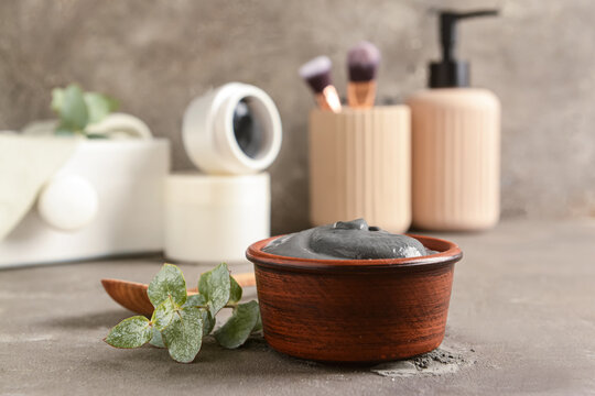 Bowl of activated carbon facial mask and eucalyptus branch on grunge background