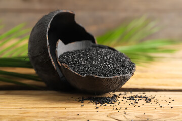 Coconut shells with activated carbon on wooden background