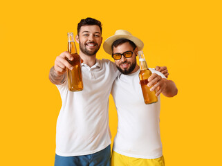 Young men with bottles of beer on yellow background