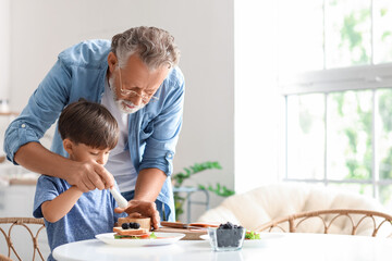 Little boy cooking with his grandfather at table in kitchen