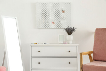 White chest of drawers with lavender bouquet and peg board on light wall background