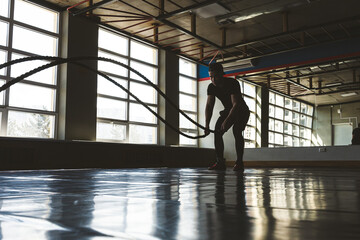 Fototapeta premium Crossfit with ropes. The athlete is training in the gym. Silhouette photography