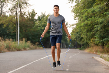 Sporty young man jumping rope outdoors