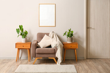 Soft armchair and wooden tables with houseplants near light wall