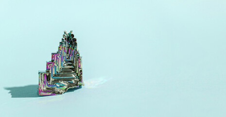 Synthetic bismuth Bismuthum crystal with iridescent oxide film on blue background close up...