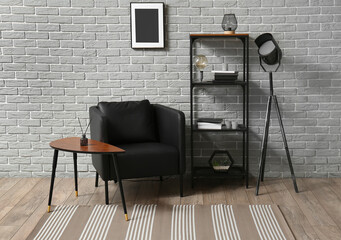 Interior of room with comfortable armchair, shelf unit and modern carpet near grey brick wall