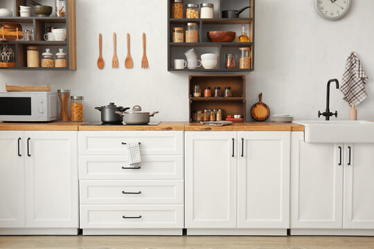 Interior of light modern kitchen with white counters and shelves