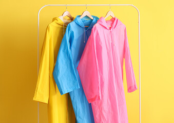 Rack with colorful raincoats near yellow wall
