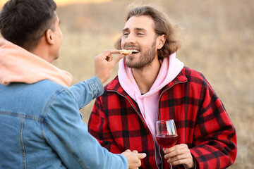 Happy gay couple having picnic outdoors on autumn day