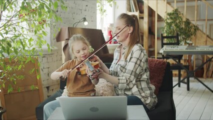 Woman helping her daughter to play violin and talking to music teacher via laptop - Powered by Adobe