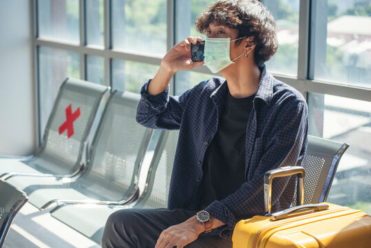 Asian young man traveller new normal wearing face mask sitting Social distancing holding smartphone in Airplane lounge. New normal Male travel pandemic passenger by plane. Coronavirus tourism trip