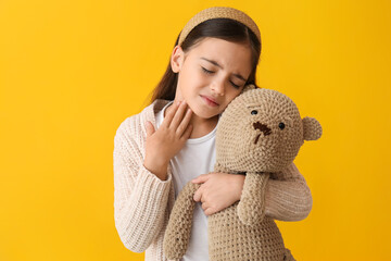Sad little girl with toy suffering from sore throat on yellow background