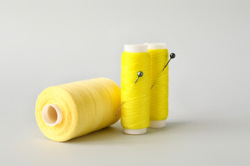 Yellow sewing thread spools with pins on light background