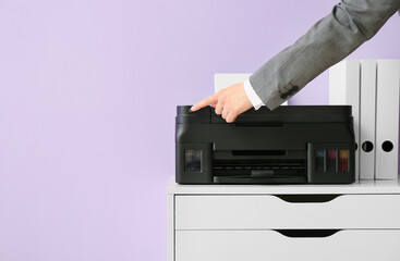 Businesswoman using modern printer on chest of drawers near color wall