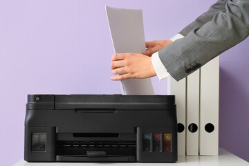 Businesswoman with paper, modern printer and folders on table near color wall