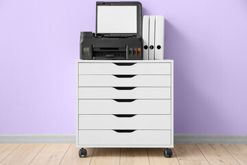 Modern copy machine and folders on chest of drawers near color wall
